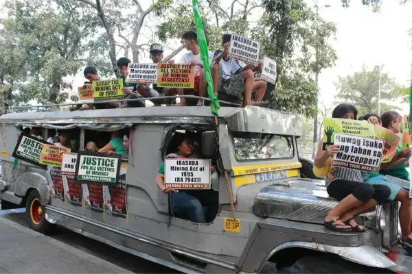Protesters on a jeepney hold signs: "Justice for all victims of mining!", "Scrap Mining Act of 1995", "Marcopper Settlement!".