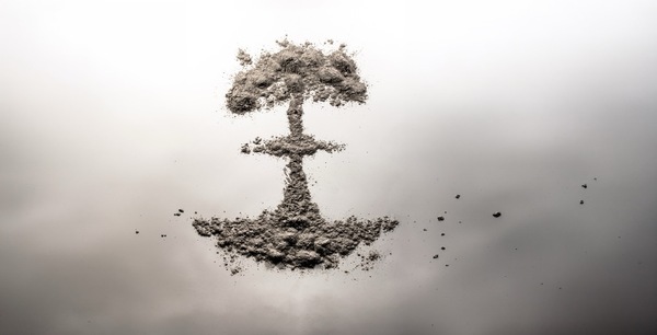 A formation of gray ash resembling a mushroom cloud or tree on a white to dark gray gradient background.