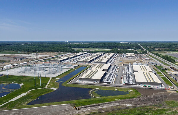 Aerial view of a large data center complex with many rectangular buildings, a power substation, nearby ponds, and a highway.